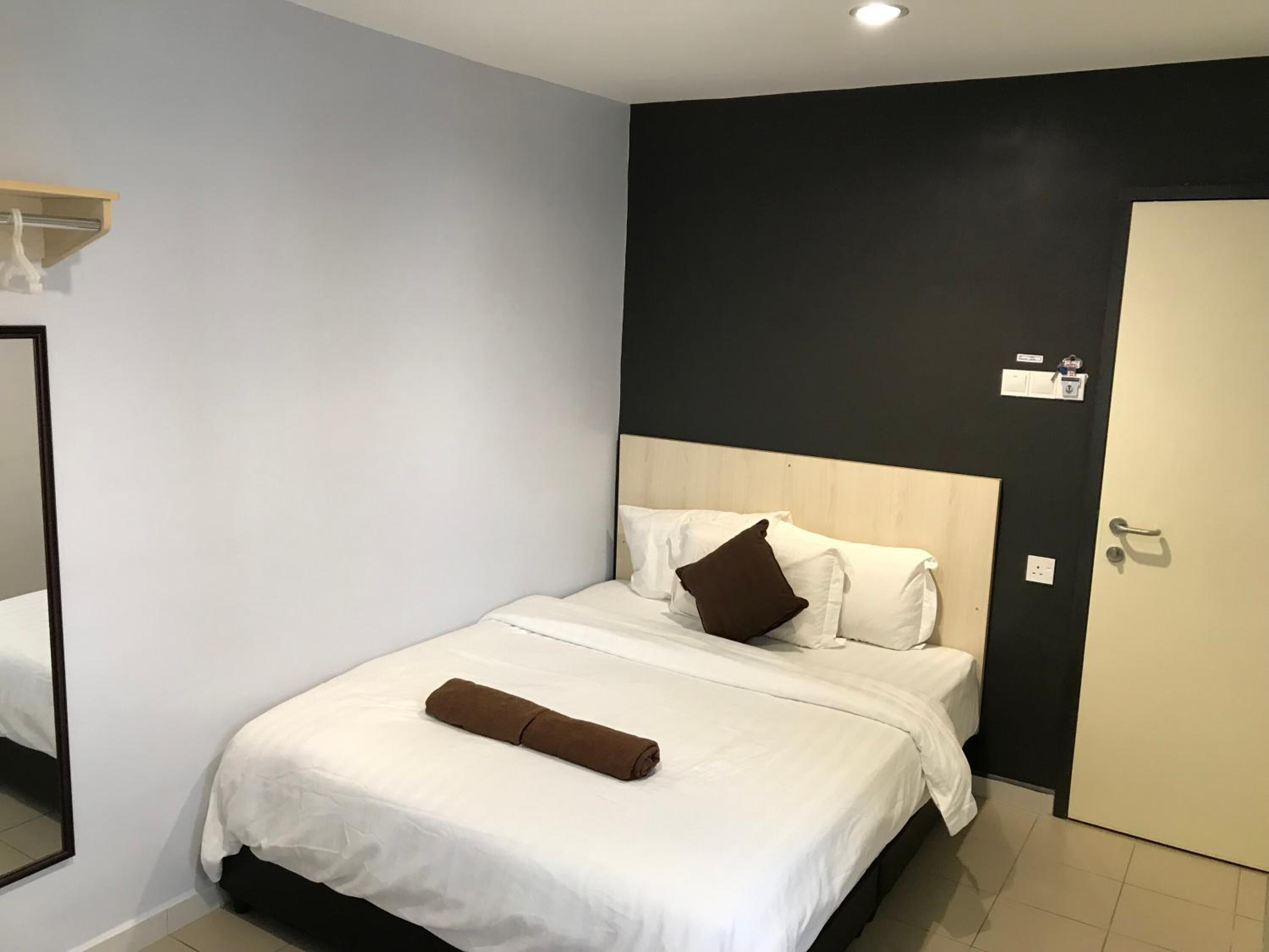 Een hotelkamer met een bed, een spiegel, een deur en een muur met een lichtschakelaar.
