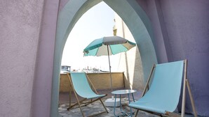 Een terras met twee blauwe loungestoelen en een tafel, beschut onder een grote parasol.