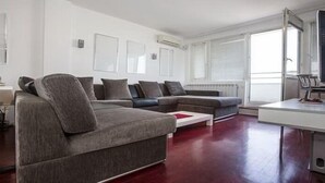 A modern living room with a grey sectional sofa, a white coffee table, and a flat-screen TV on a stand. - Apartment Sunset (Belgrade)