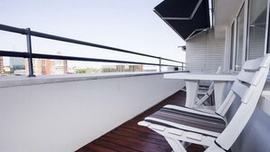 A balcony with a white table and chair, a black railing, and a view of buildings in the background. - Apartment Sunset (Belgrade)