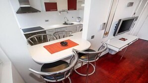 A compact kitchen with a dining area, including a table with chairs, a small island, and a TV. - Apartment Sunset (Belgrade)