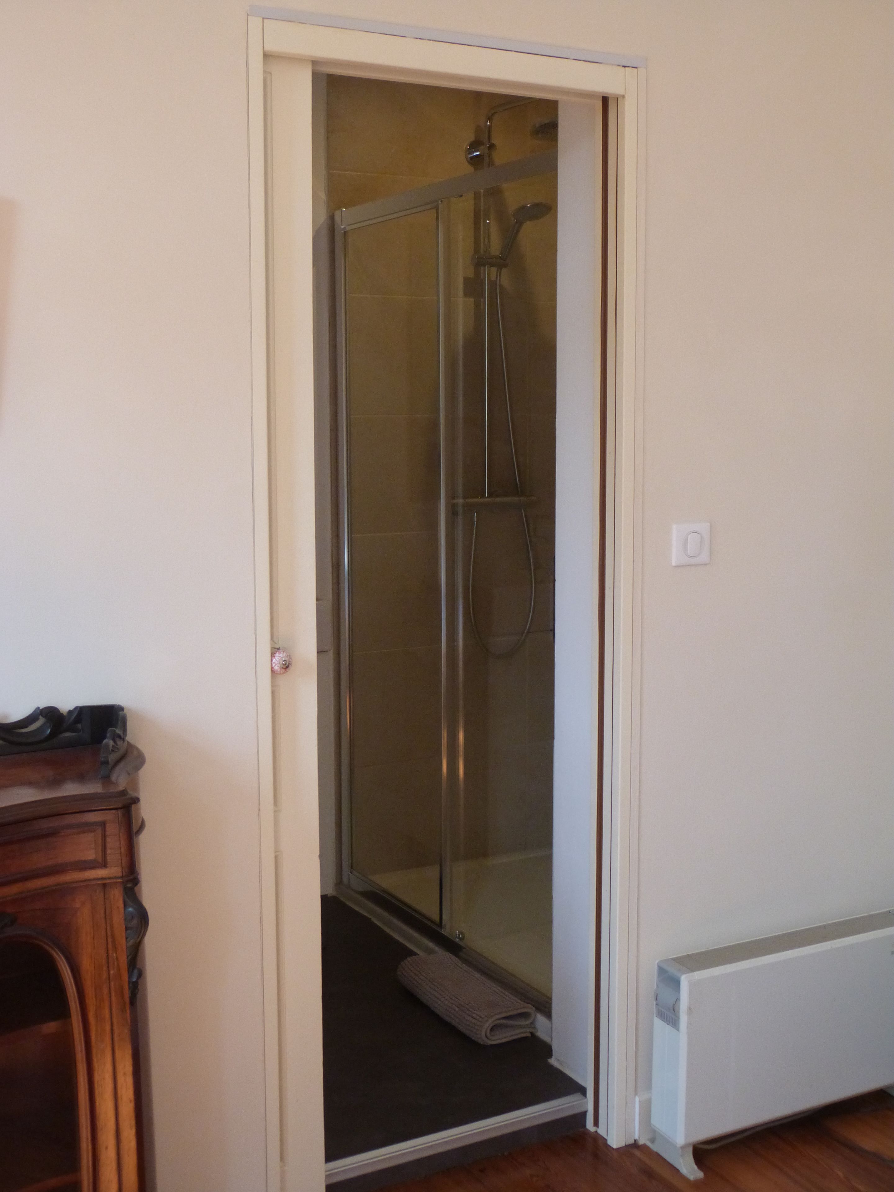 A glass-enclosed shower area with a door leading to a room.