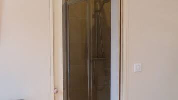 A glass-enclosed shower area with a door leading to a room.