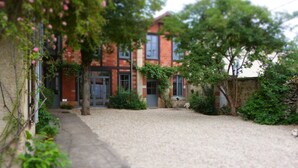 Un bâtiment à la façade en briques, une allée gravillonnée et un chemin menant à l’entrée.