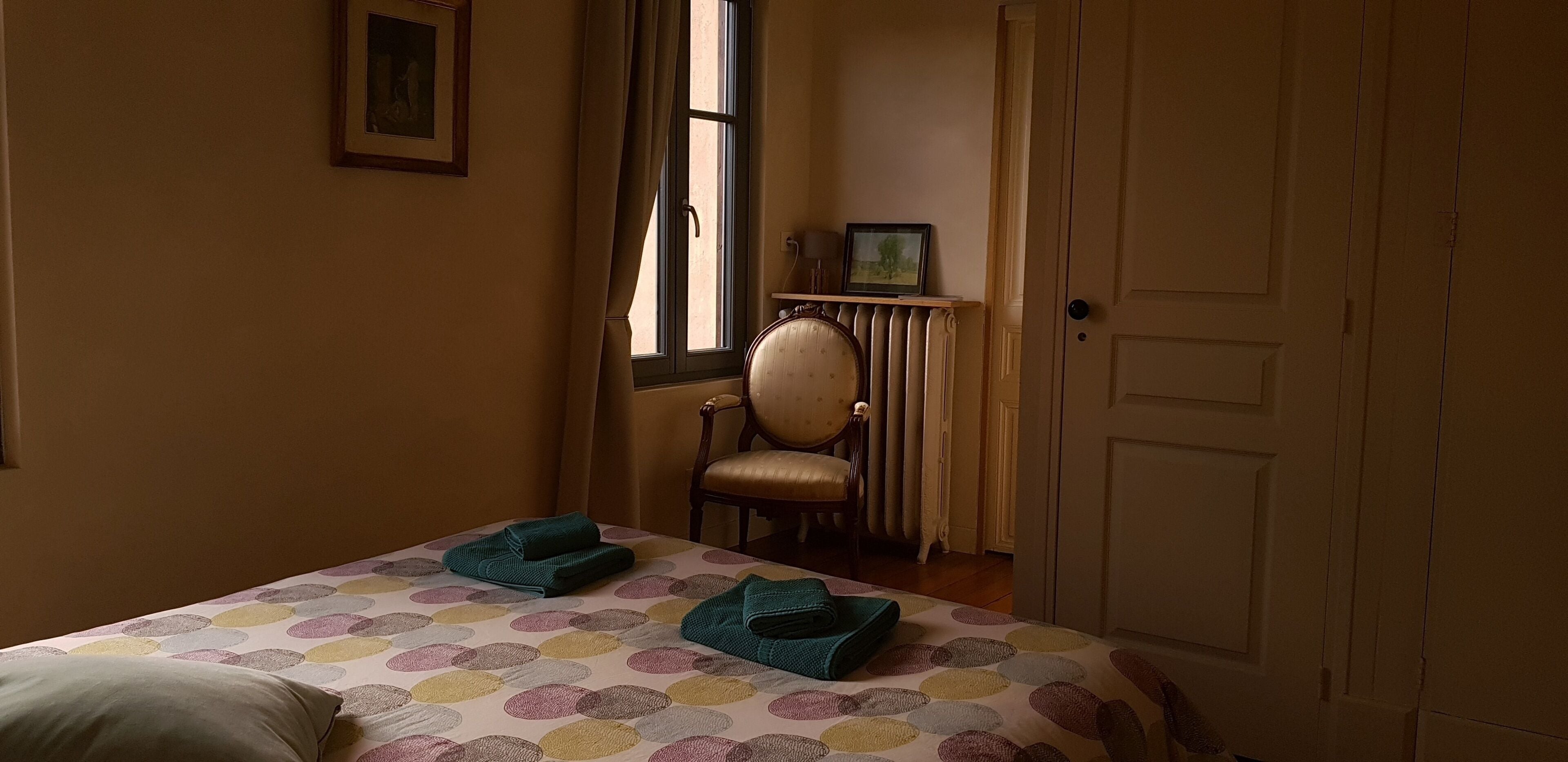 A bedroom with a bed, a chair, a radiator, and a door.