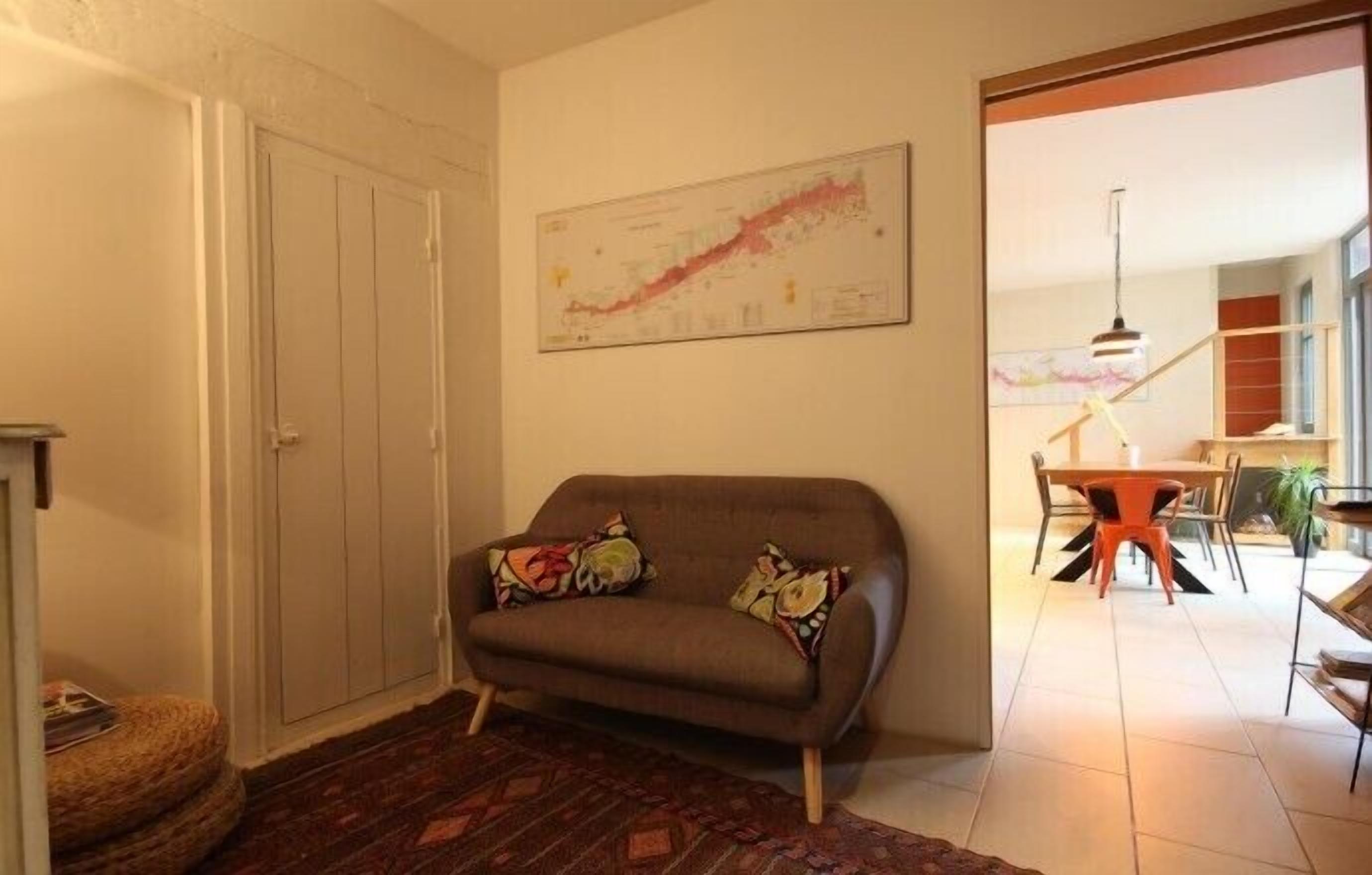 Un salon comprenant un canapé, un tapis à motifs, un coin repas avec une table et des chaises, et un escalier menant à un autre niveau.