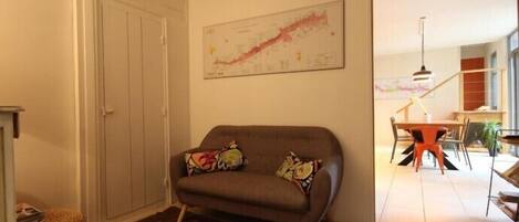 Una sala de estar con un sofá, un tapete estampado, un comedor con mesa y sillas, y una escalera que sube a otro nivel.