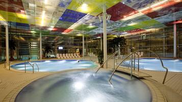 An indoor swimming pool with multiple lanes, surrounded by lounge chairs and a glass wall.
