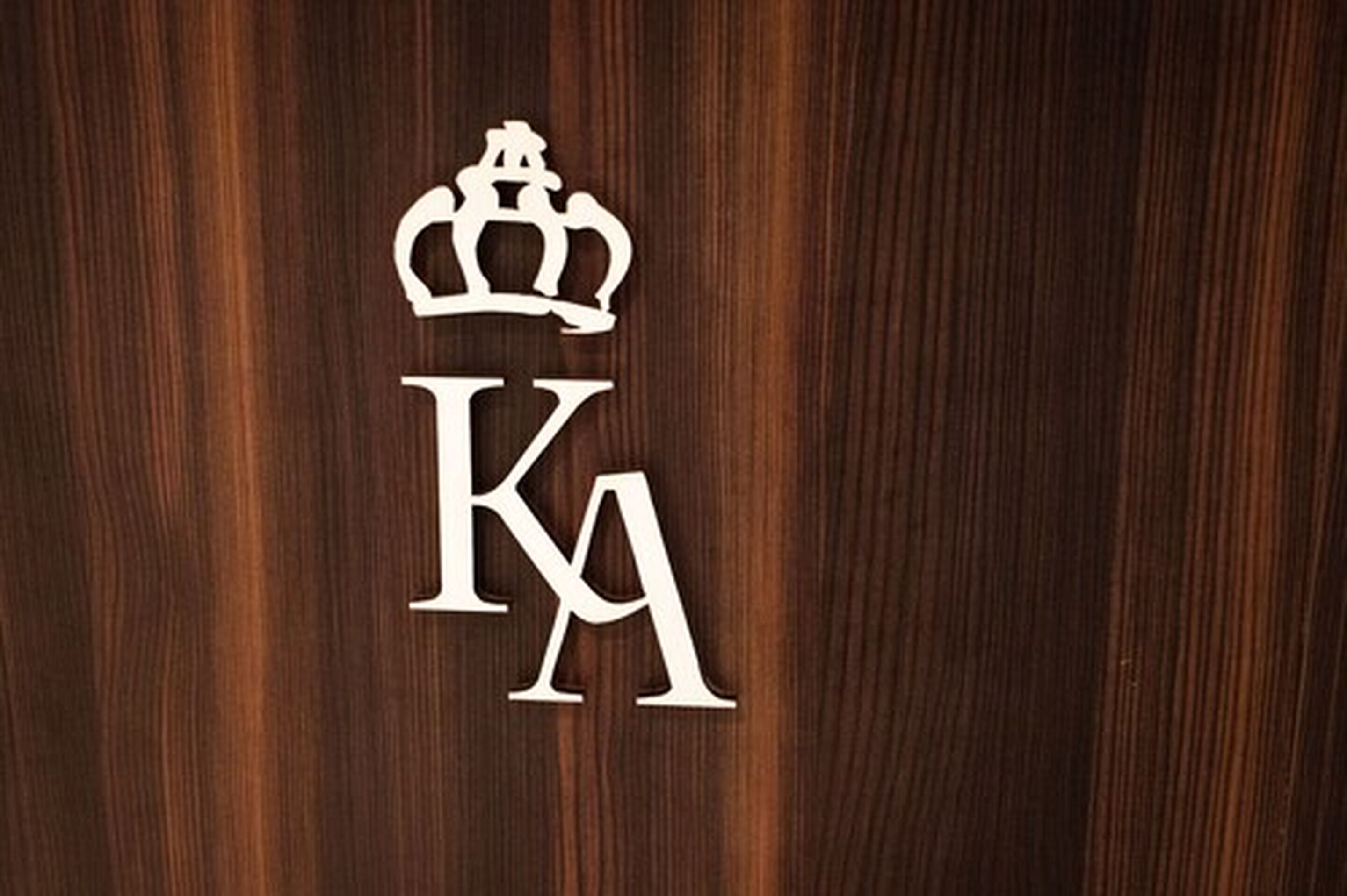 Una superficie de madera con un logotipo blanco en relieve que muestra una corona sobre las letras "KA".