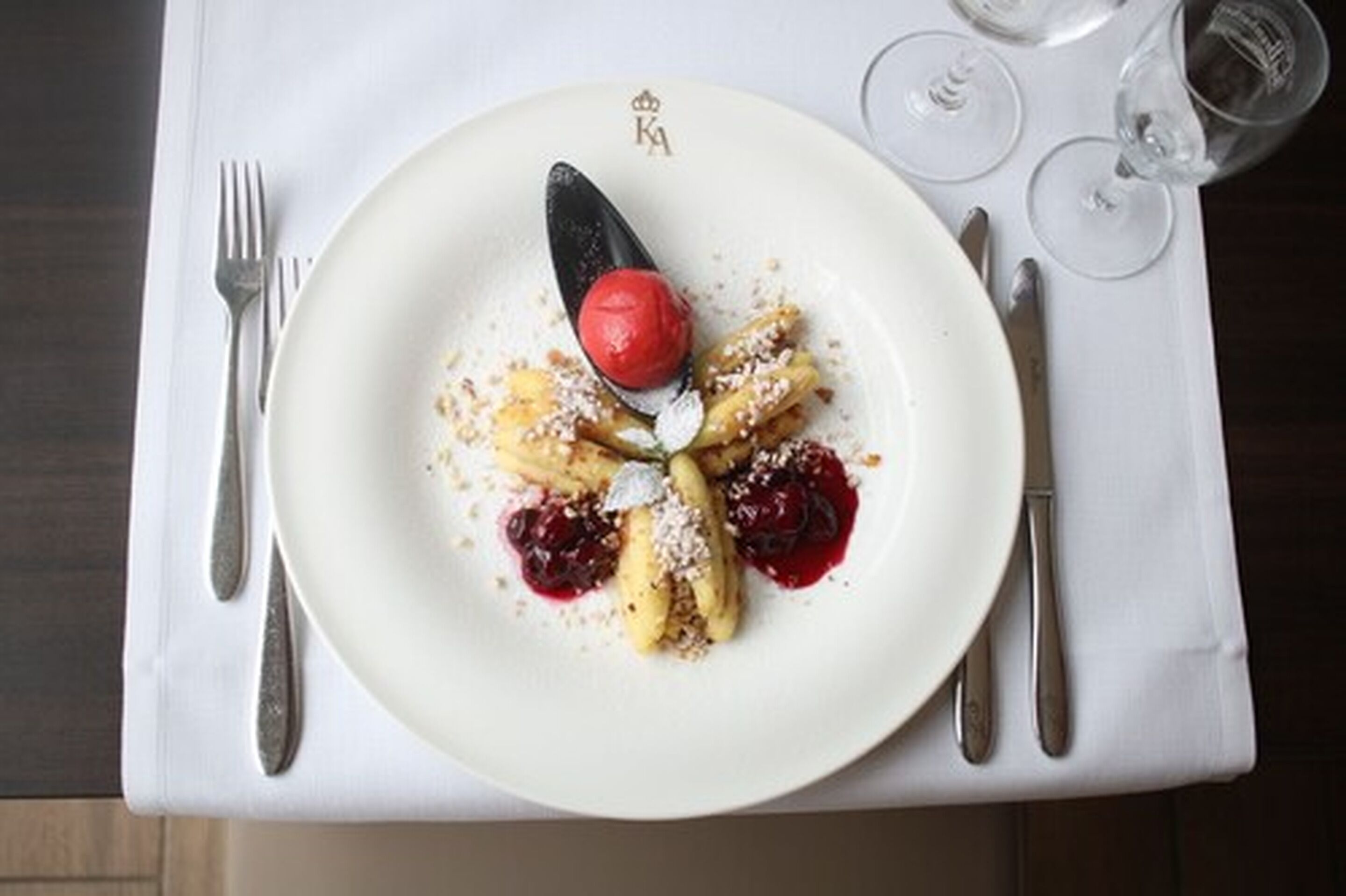 A plate of dessert with a cherry on top, accompanied by a fork and knife on a white napkin.