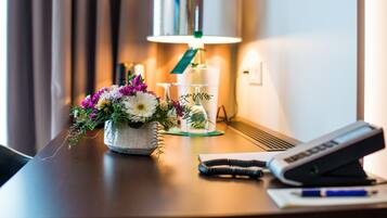 A desk with a lamp, a floral arrangement, a glass, a pen, and a phone.