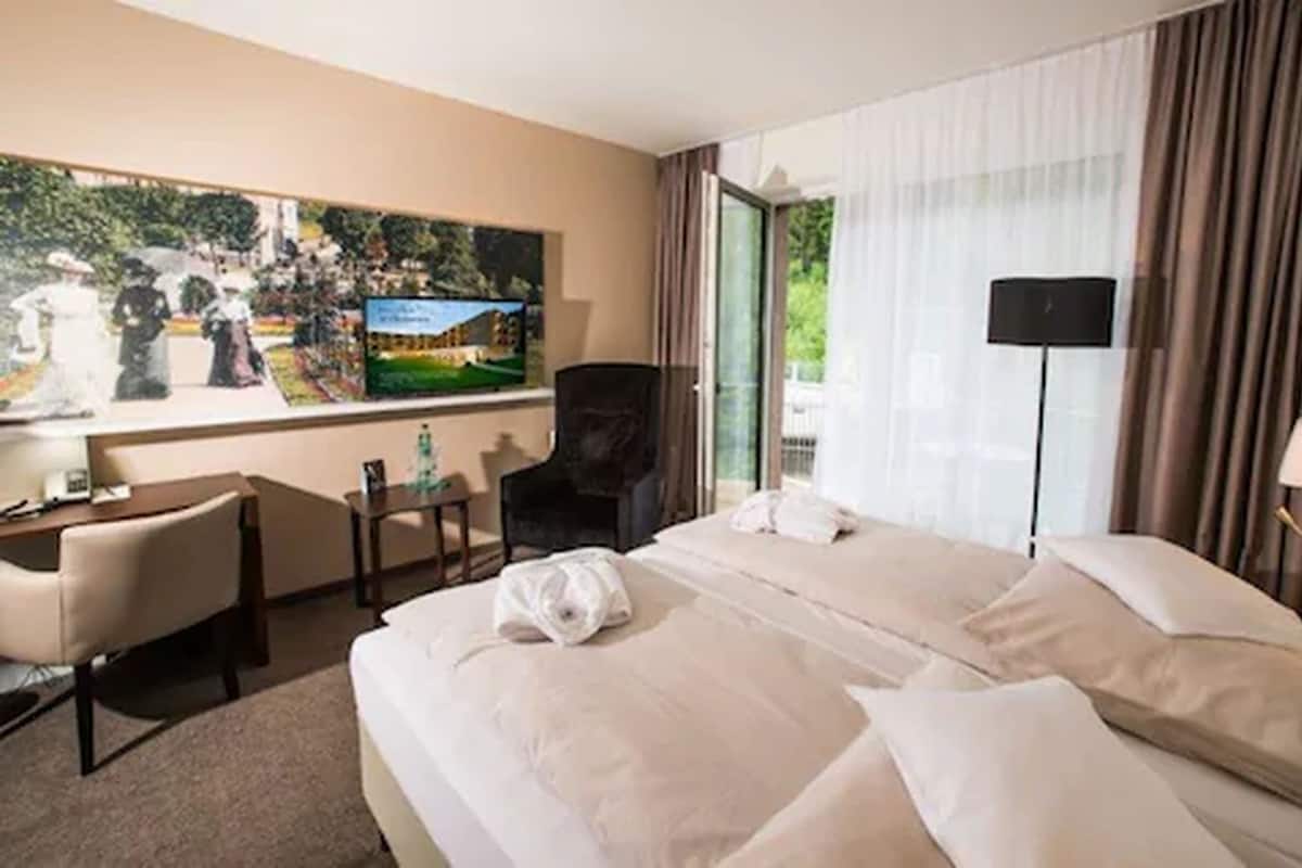 A hotel room with a large bed, a desk, a chair, a television, and a window with curtains.