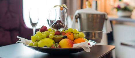 A fruit bowl on a table with a pitcher of water and a coffee maker in the background.