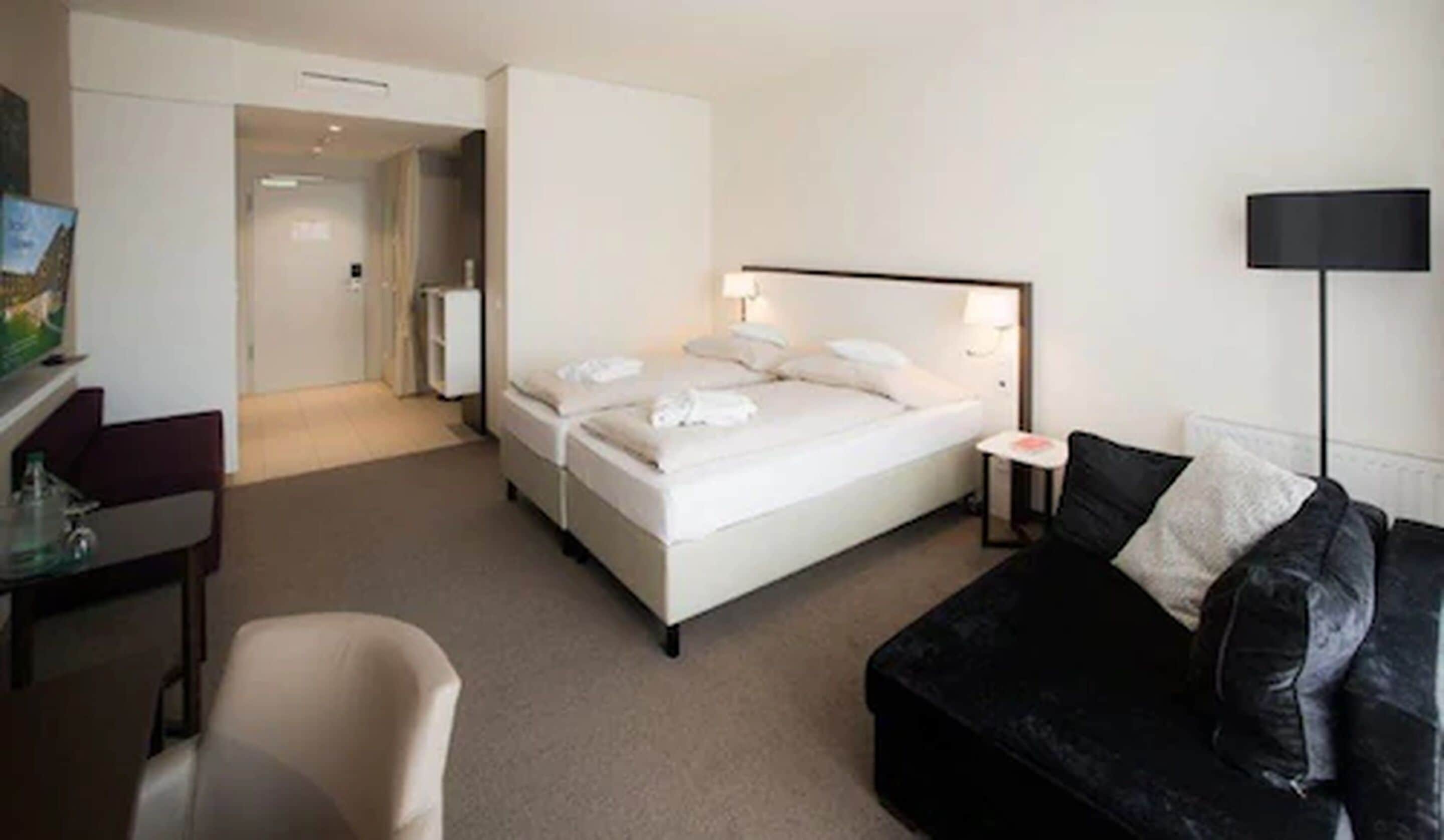 Ein Hotelzimmer mit Bett, Schreibtisch, Stuhl, einer schwarzen Ledersofa und einer Lampe.