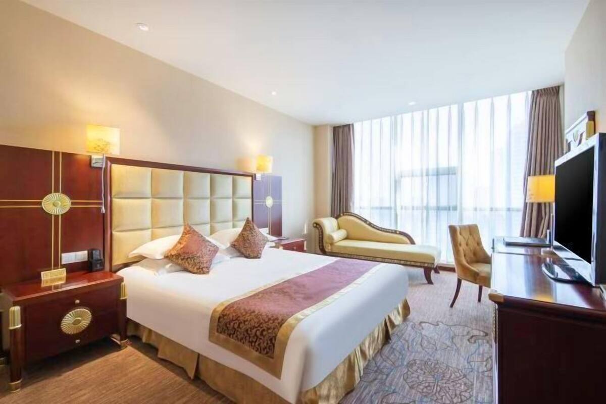 Ein Hotelzimmer mit einem großen Bett, einem Schreibtisch, einem Sessel, einem Fernseher und einem Fenster mit Vorhängen.