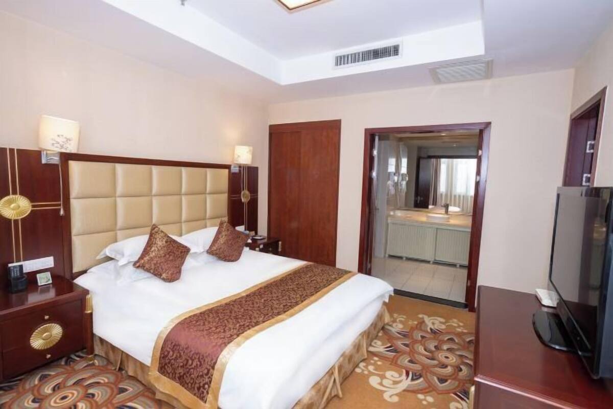 Ein Hotelzimmer mit einem großen Bett, einem Fernseher, einem Schreibtisch und einem durch eine offene Tür einsehbaren Badezimmer.