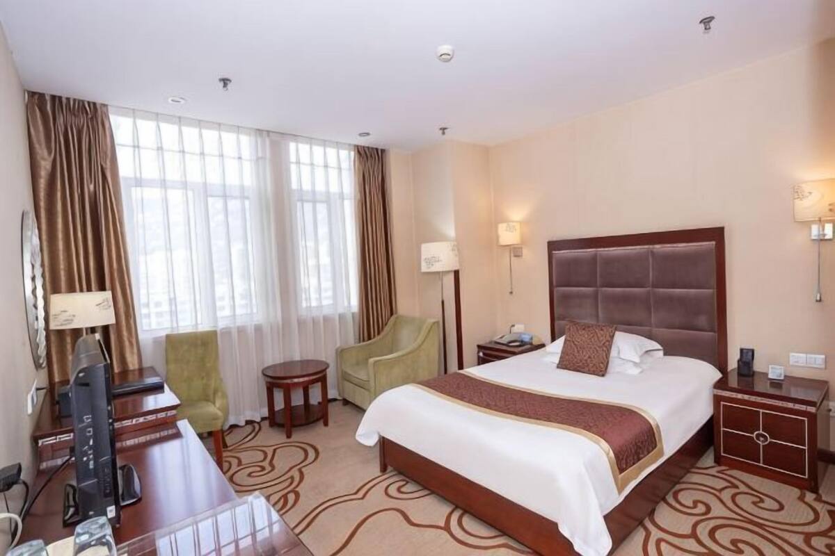 Ein Hotelzimmer mit einem großen Bett, einem Schreibtisch mit Computer, einem Sessel, einem kleinen Tisch und einem Nachttisch.