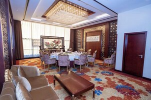 A hotel room with a dining area, a sofa set, a large rug, and a chandelier.