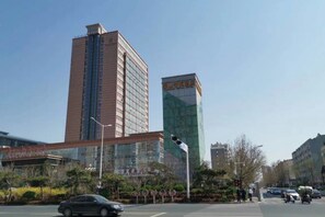 A city street with tall buildings, including a modern glass skyscraper and a traditional building with a red facade. - Taishan Royal Hotel (Tai'an)