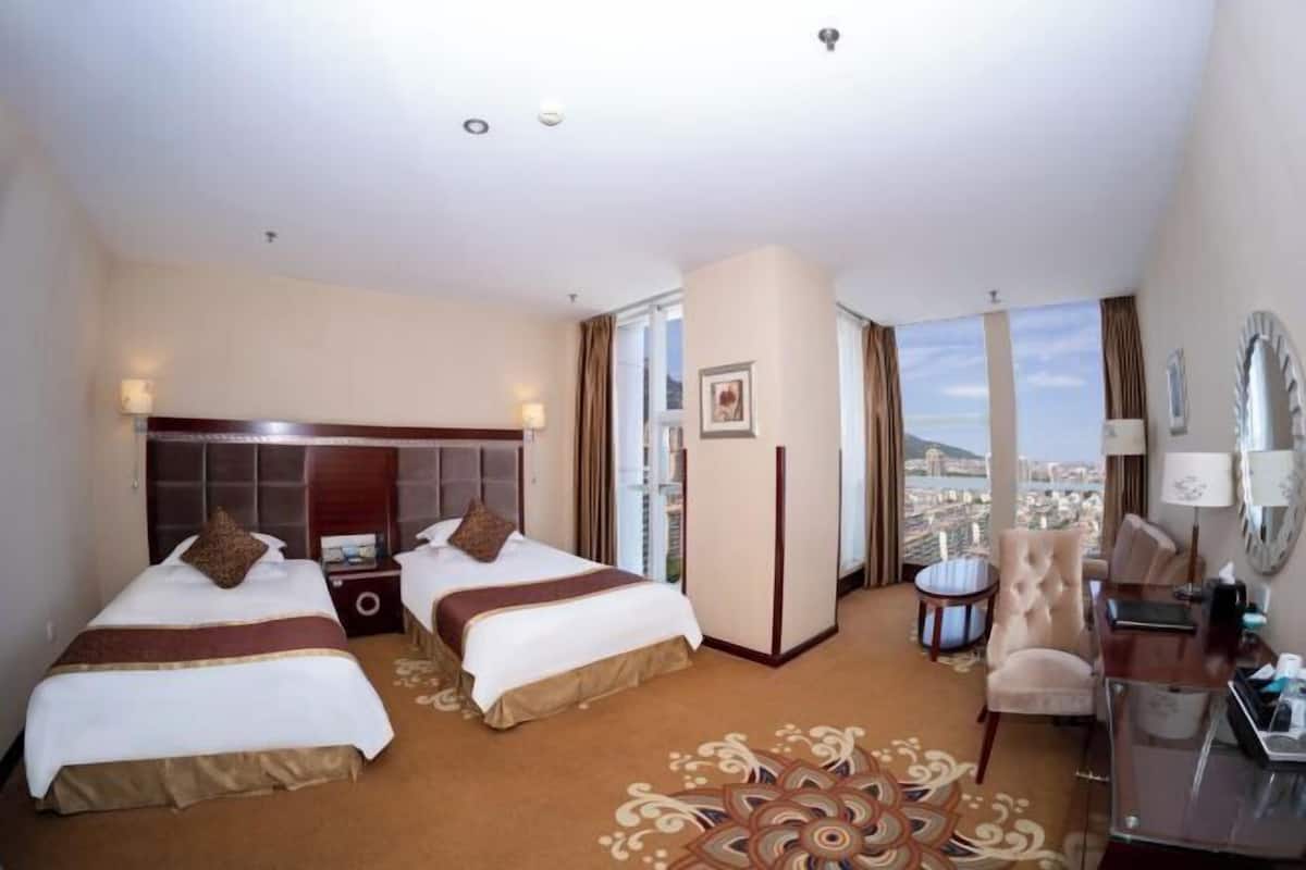 Ein Hotelzimmer mit zwei Betten, einem Schreibtisch, einem Stuhl und Blick auf die Stadt.