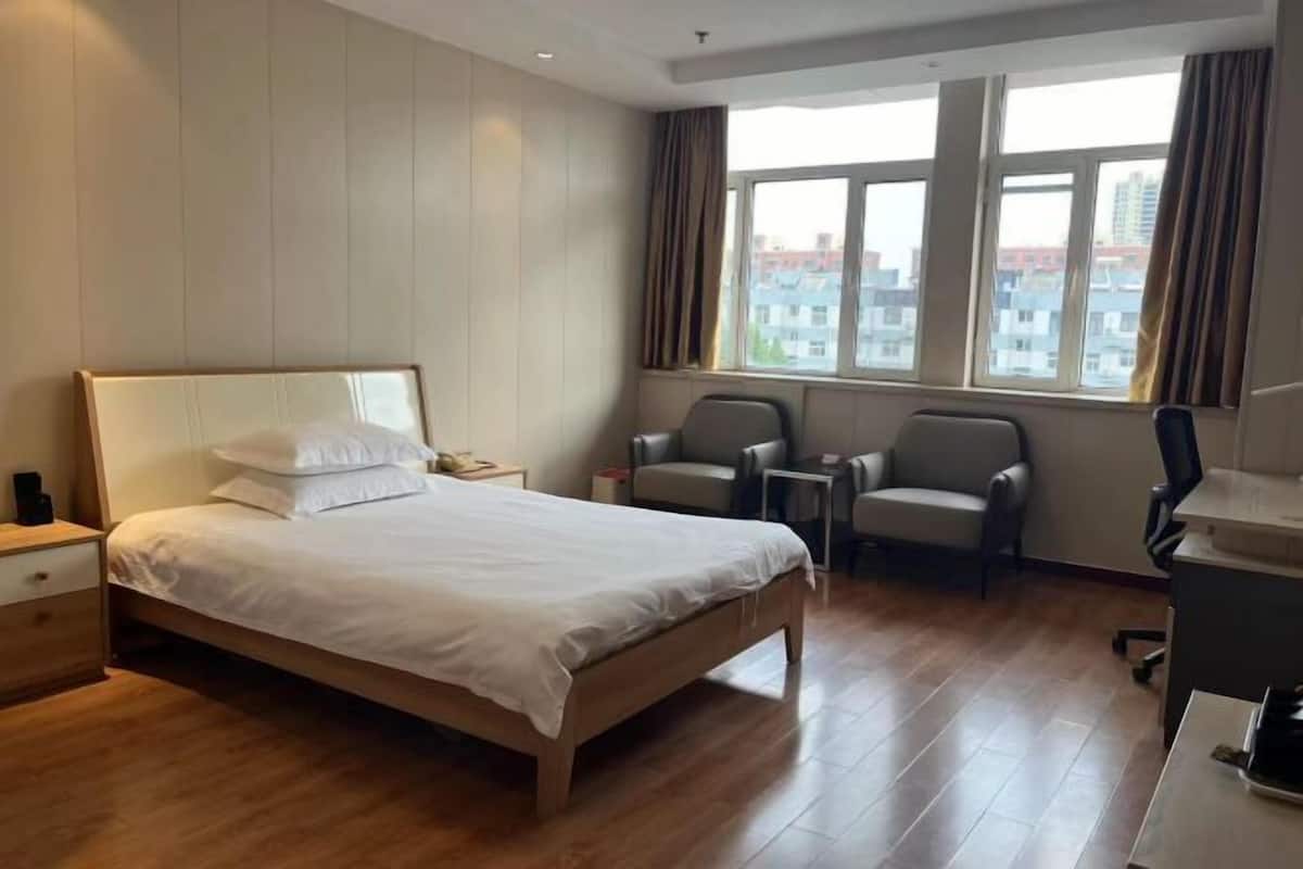 Ein Hotelzimmer mit einem großen Bett, zwei Stühlen, einem Schreibtisch und einem Fenster mit Vorhängen.