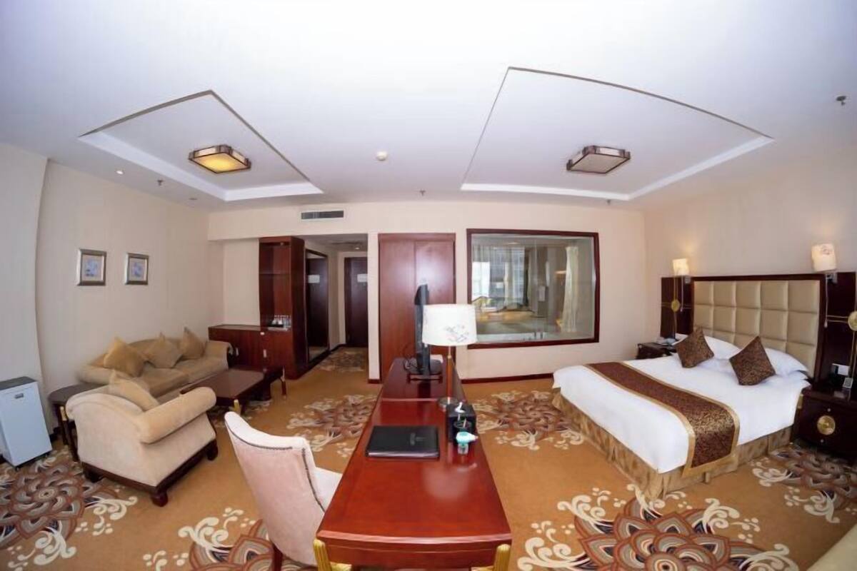 Ein Hotelzimmer mit Bett, Schreibtisch, Sofa, Sessel, kleinem Tisch und Fernseher.