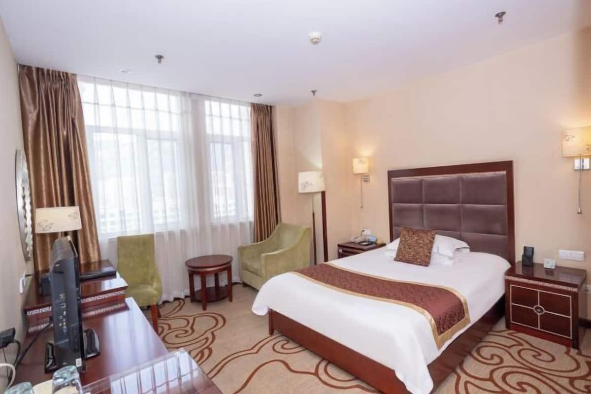 Ein Hotelzimmer mit einem großen Bett, einem Schreibtisch, einem Stuhl, einer Lampe und einem Fernseher.