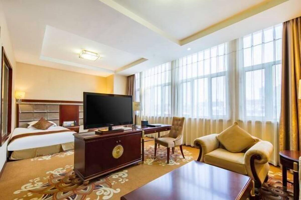 Ein Hotelzimmer mit einem Bett, einem Schreibtisch, einem Fernseher, einer Couch und großen Fenstern.