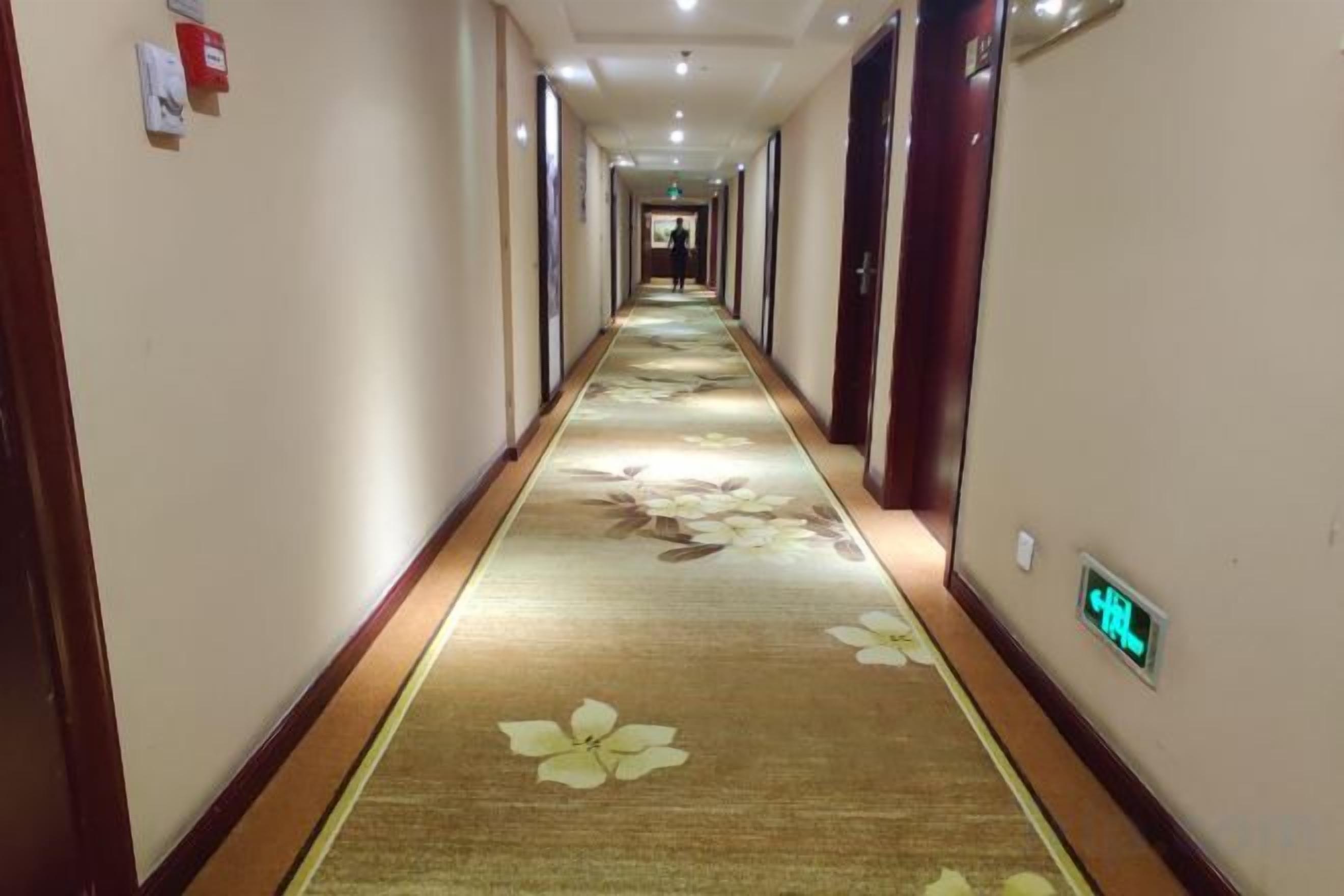 Ein Hotelgang mit Teppichboden, Türen auf beiden Seiten und einem digitalen Schild an der Wand.