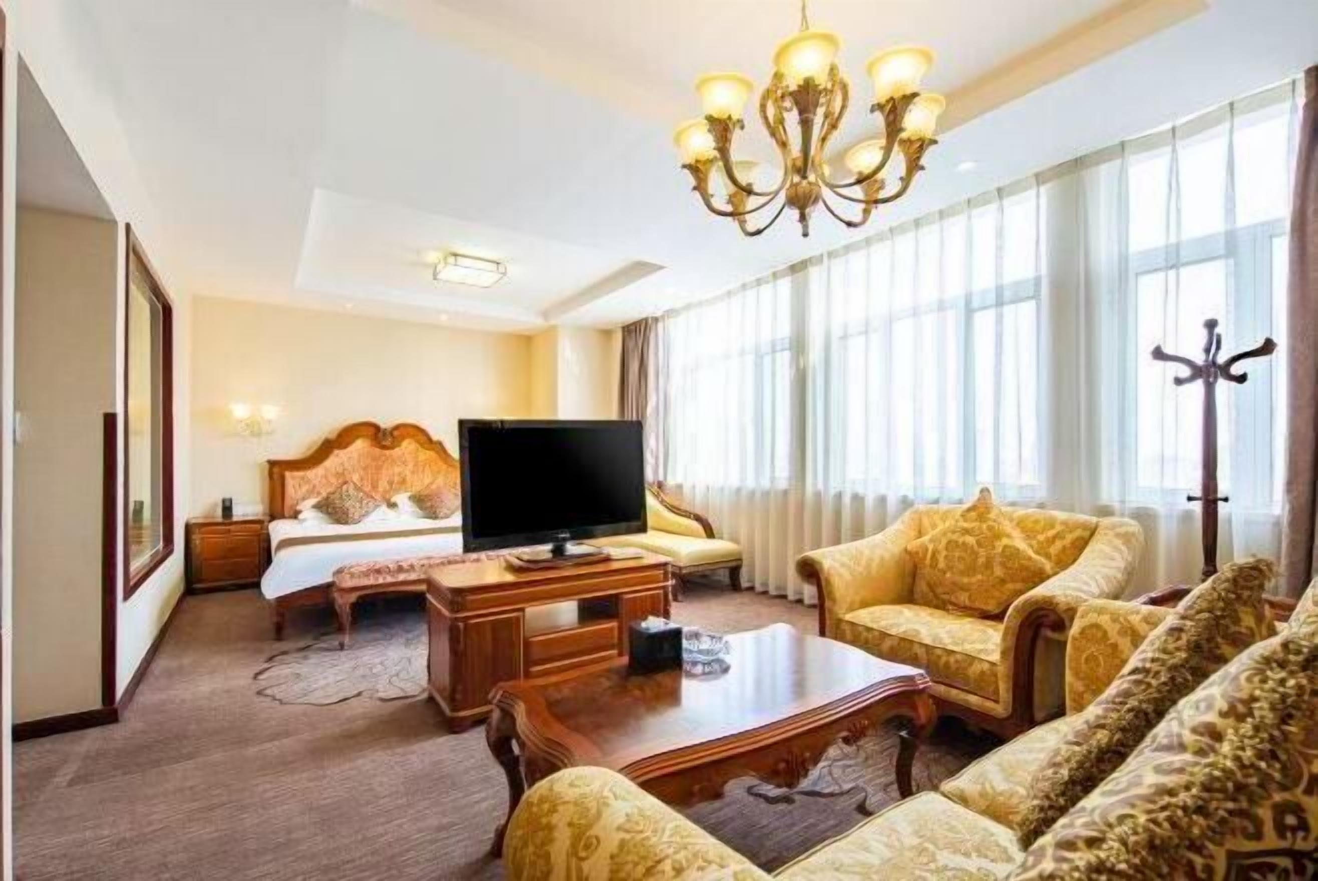 Quarto de hotel com uma cama, televisão, mesa de centro de madeira e duas poltronas estampadas.