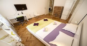 A hotel room with a bed, a desk with a chair, a television, and a fireplace.