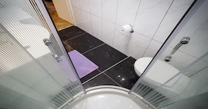 A modern bathroom with a glass shower enclosure, a white toilet, and a black tiled floor.