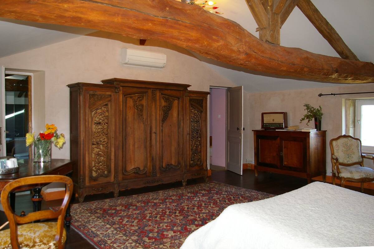 Une chambre avec un grand lit, une armoire en bois et un coin repas comprenant une table et des chaises.