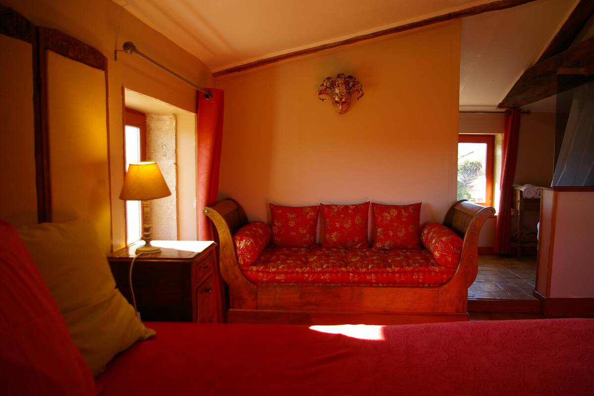 Une pièce chaleureuse avec un canapé en bois, une table de chevet avec une lampe et une couverture rouge sur le lit.