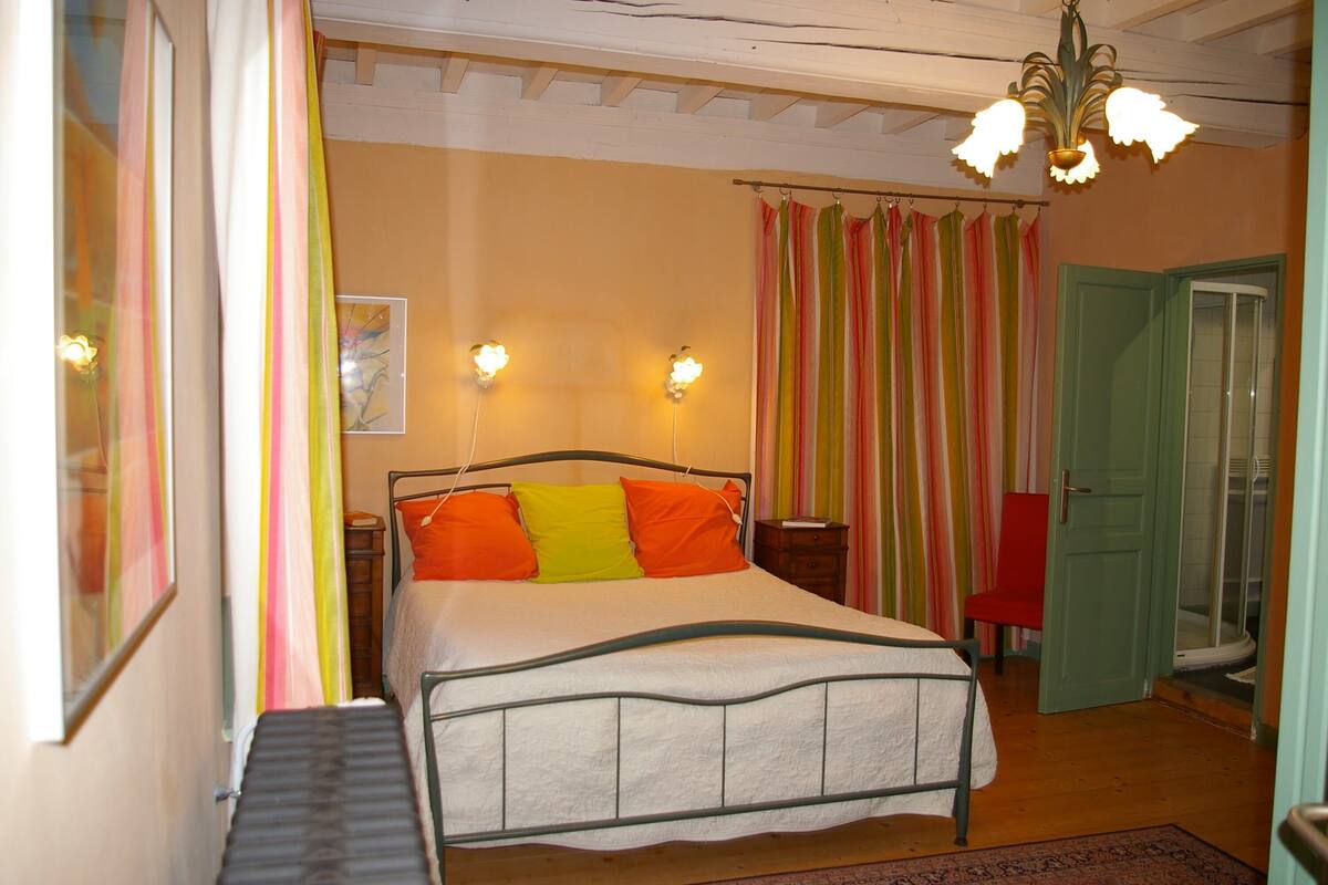 Une chambre à coucher comprenant un lit, une chaise, une table de chevet et une porte donnant sur une salle de bain.
