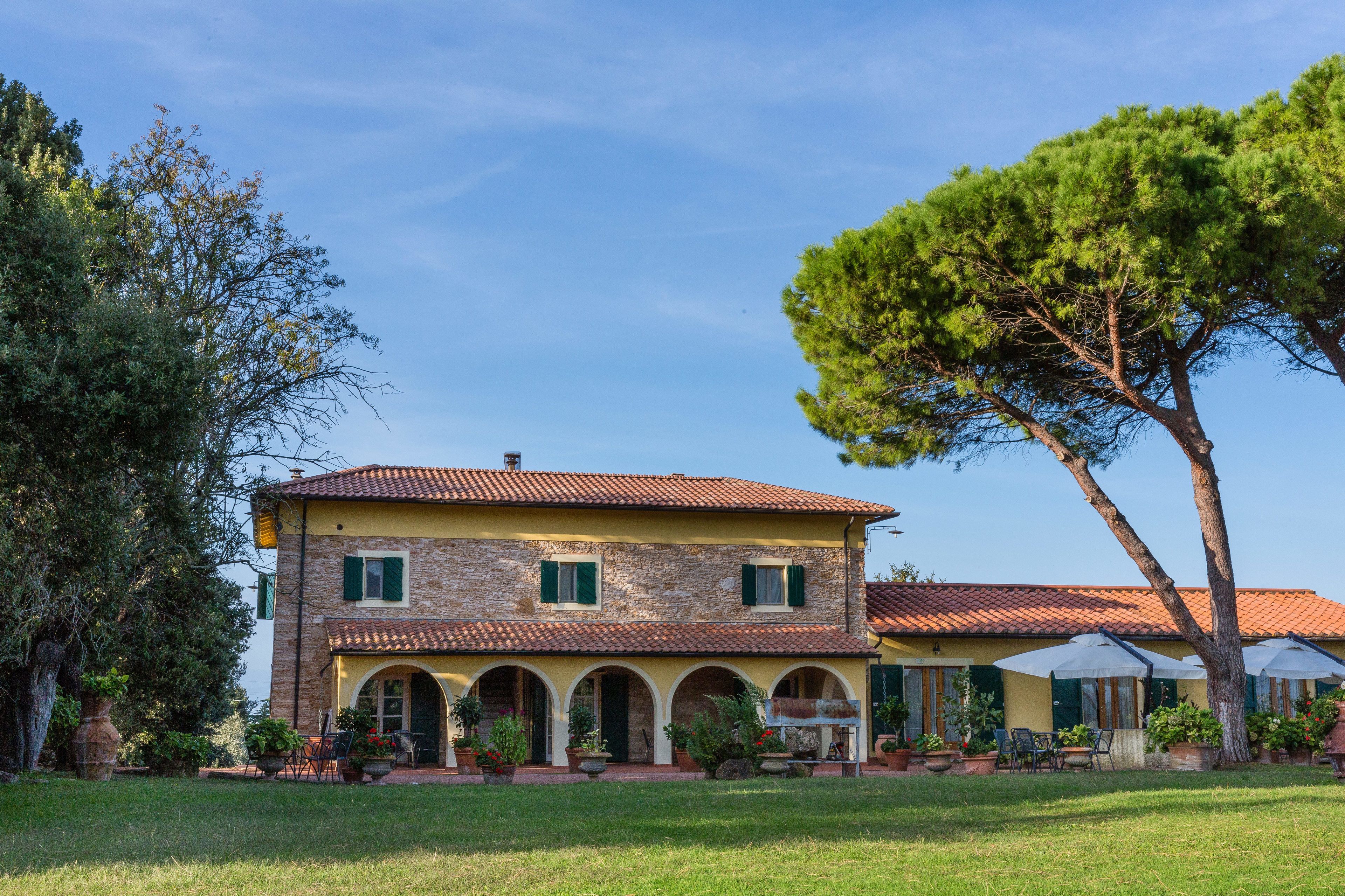 A two-story stone building with a tiled roof, arched windows, and a courtyard with outdoor seating.