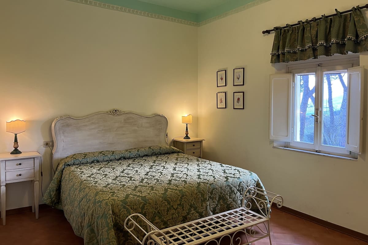 Een slaapkamer met een bed, nachtkastjes, een raam met gordijnen en aan de muur hangende foto's.