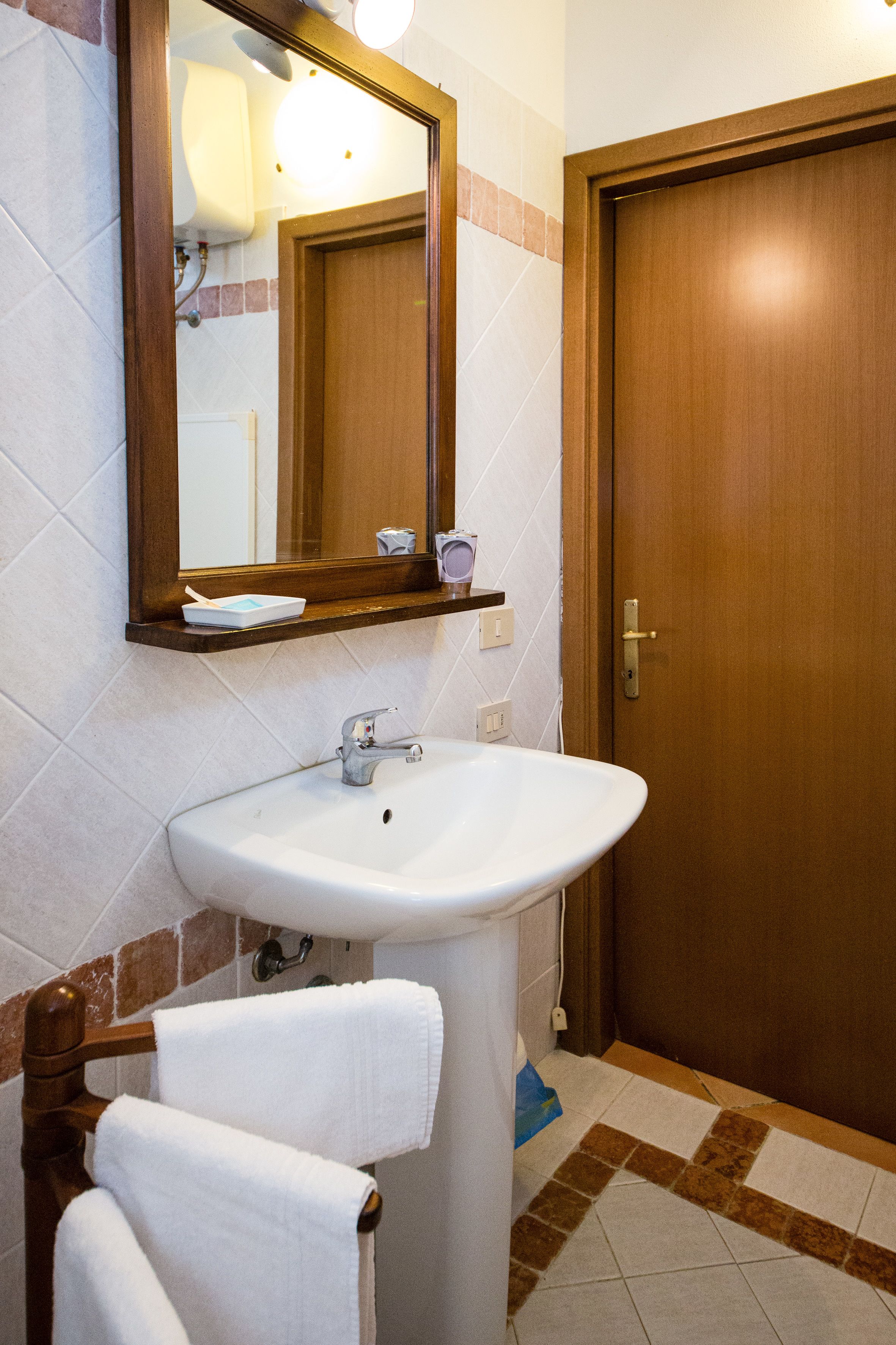 Ein Badezimmer mit einem weißen Waschbecken, einer Holztür und einem Spiegel über dem Waschbecken.