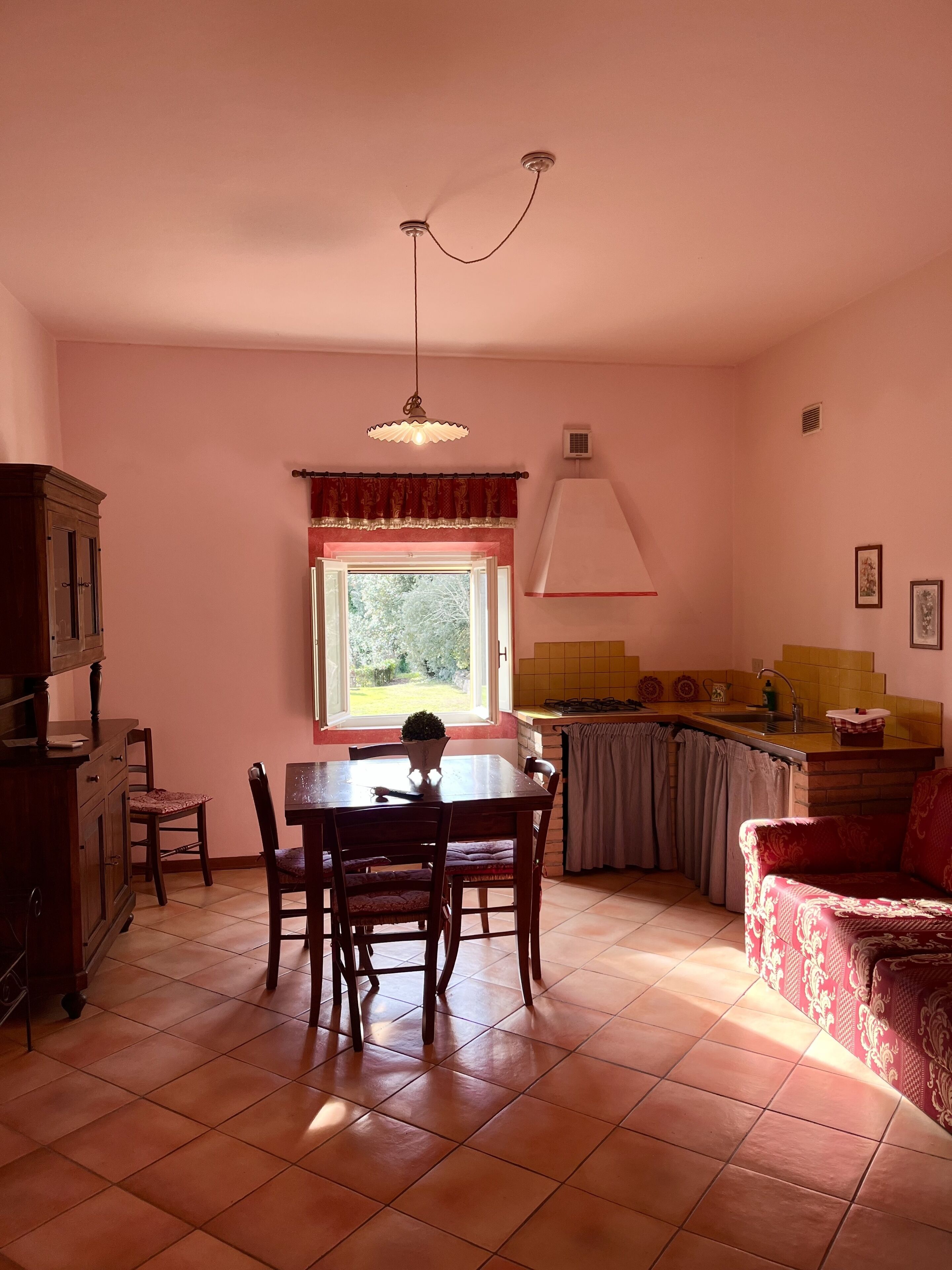Een gezellig eetgedeelte met een tafel en stoelen, een raam met uitzicht, een keuken met een spoelbak en fornuis, en een rode bank.
