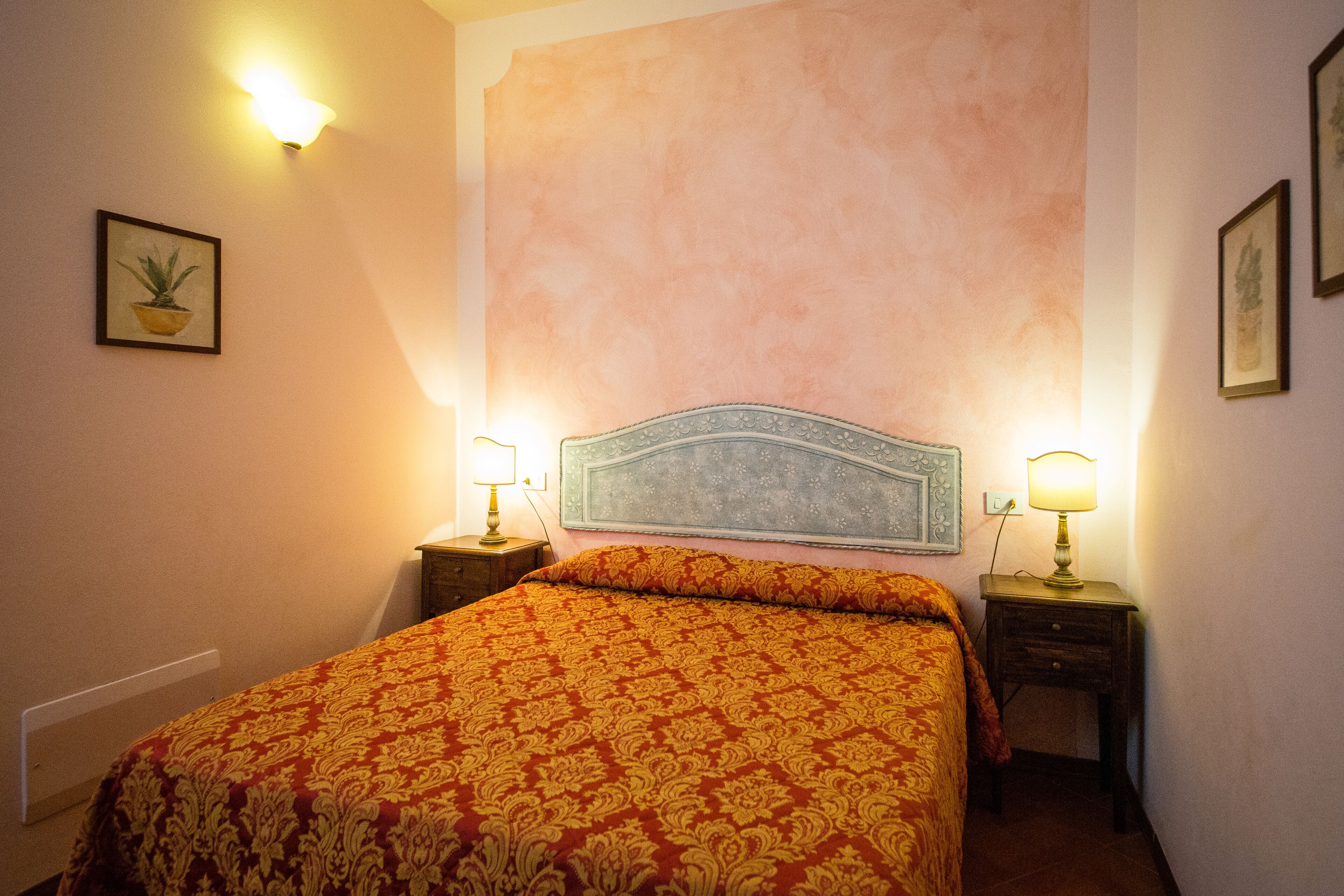 A bedroom with a large bed, two bedside tables with lamps, and a wall-mounted light fixture.