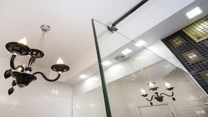 A modern bathroom with a glass shower enclosure, a black chandelier, and a visible door. - Apartment Mozaik (Belgrade)