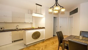 A modern kitchen with white cabinets, a wooden countertop, and a unique decorative wall piece. There is a dining area with a table and chairs. - Apartment Mozaik (Belgrade)