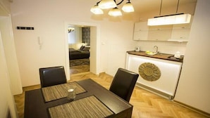 A dining area with a wooden table and chairs, a kitchen with white cabinets, and a decorative wall piece. - Apartment Mozaik (Belgrade)