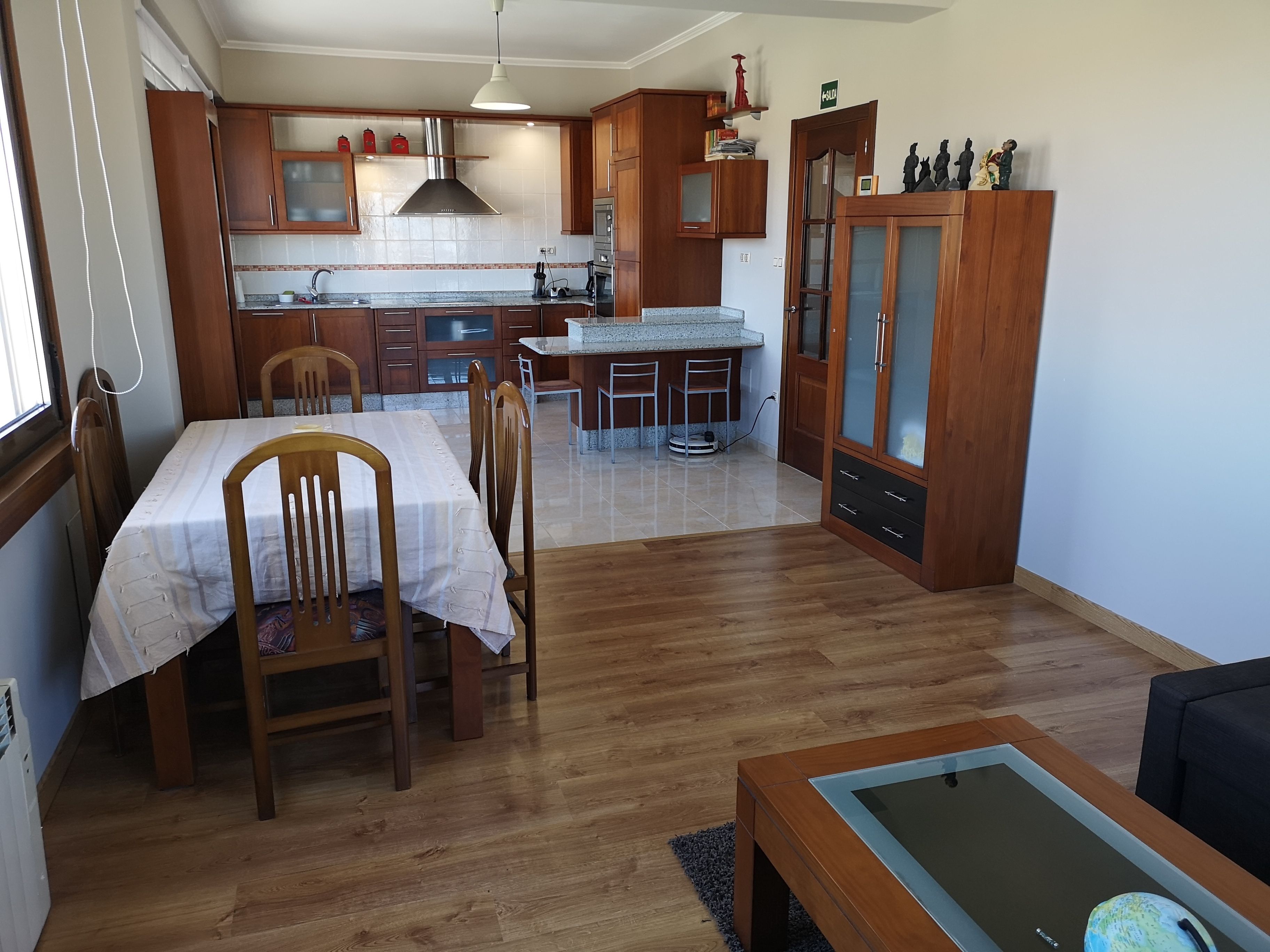 A compact kitchen with wooden cabinets, a dining table with chairs, and a small island with a sink.