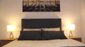 Un dormitorio con una cama grande, dos lámparas de noche y un cuadro con barcos en la pared.