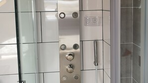 Moderni suihku, jossa on lasinen suihkuseinä, käsisuihkupää ja useita painikkeita sisältävä ohjauspaneeli.