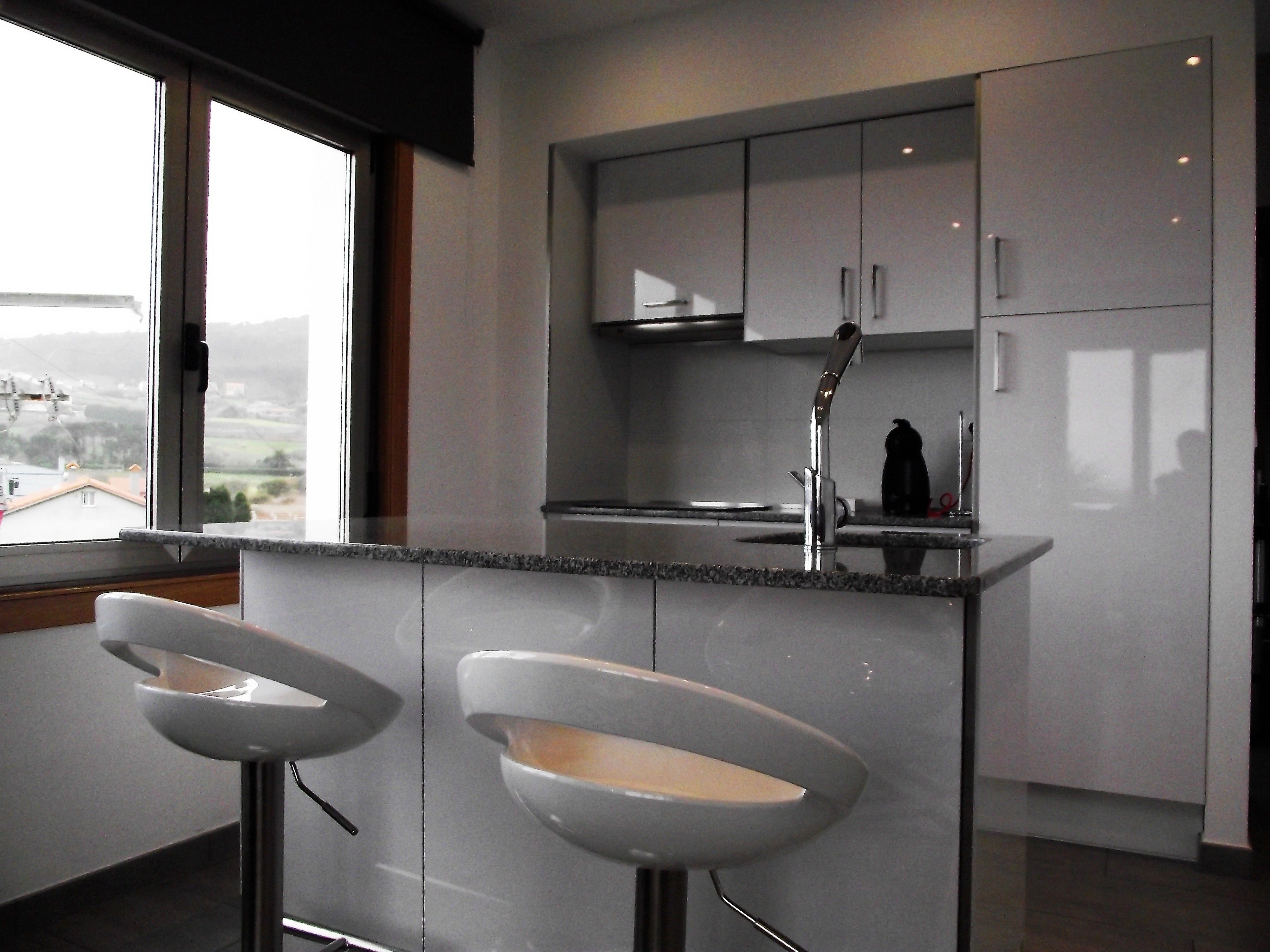 A modern kitchen with a large window, two bar stools, and stainless steel appliances.