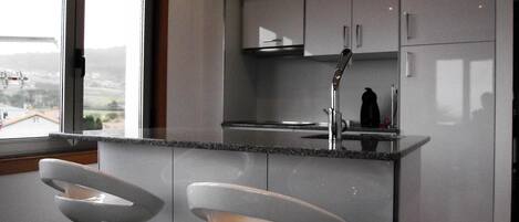 A modern kitchen with a large window, two bar stools, and stainless steel appliances.
