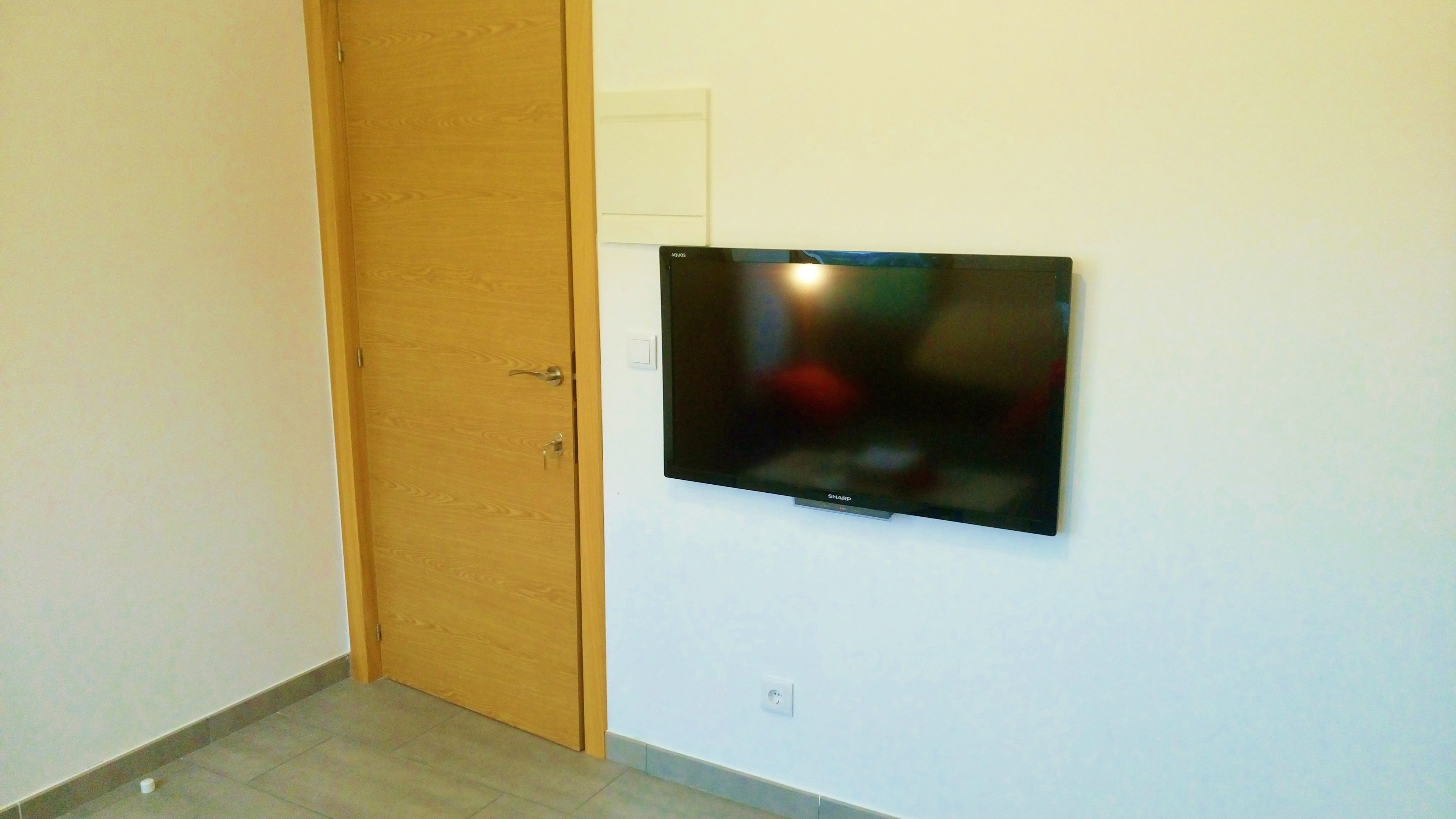 A room with a wooden door, a mounted flat-screen TV, and a light switch on the wall.