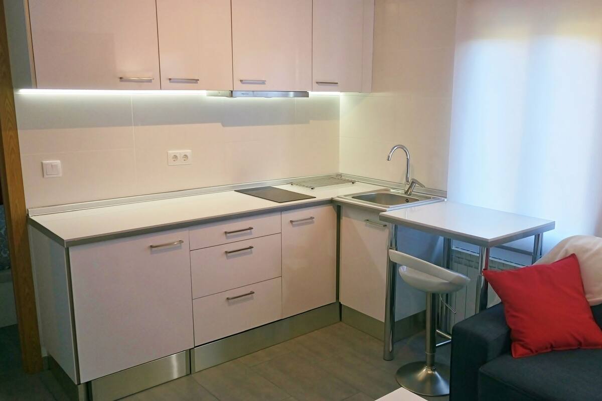 Una cocina compacta con armarios blancos, un lavamanos de acero inoxidable y un taburete de bar.
